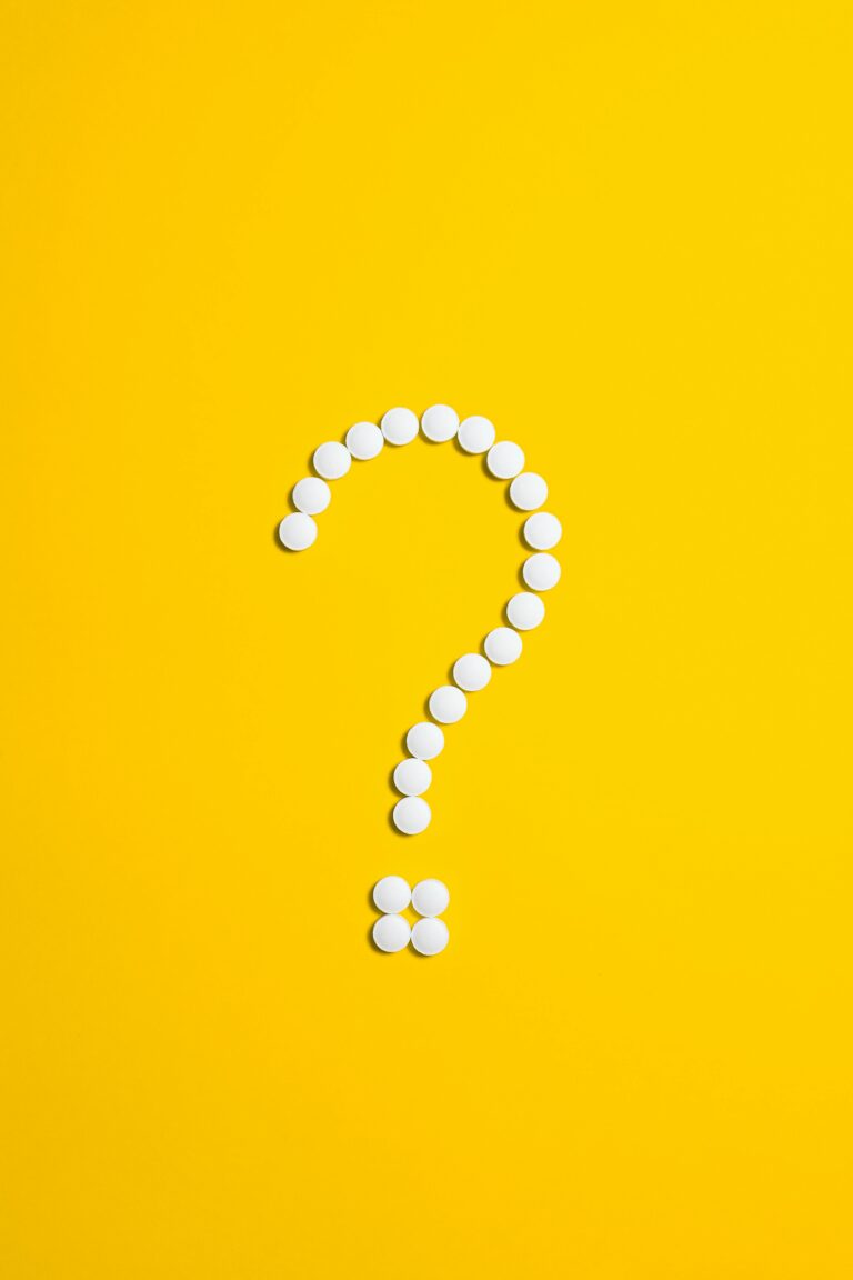 White pills arranged in a question mark shape on a bright yellow background, symbolizing medical queries.